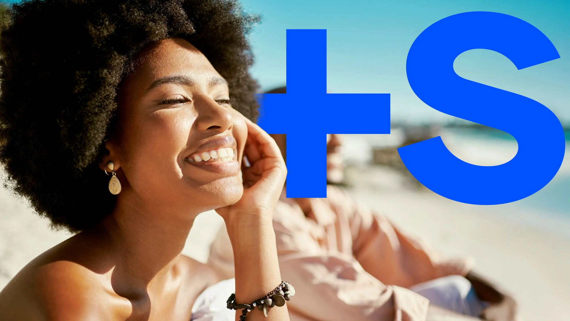 Close-up of a smiling woman with natural afro hair enjoying sunshine at a beach.