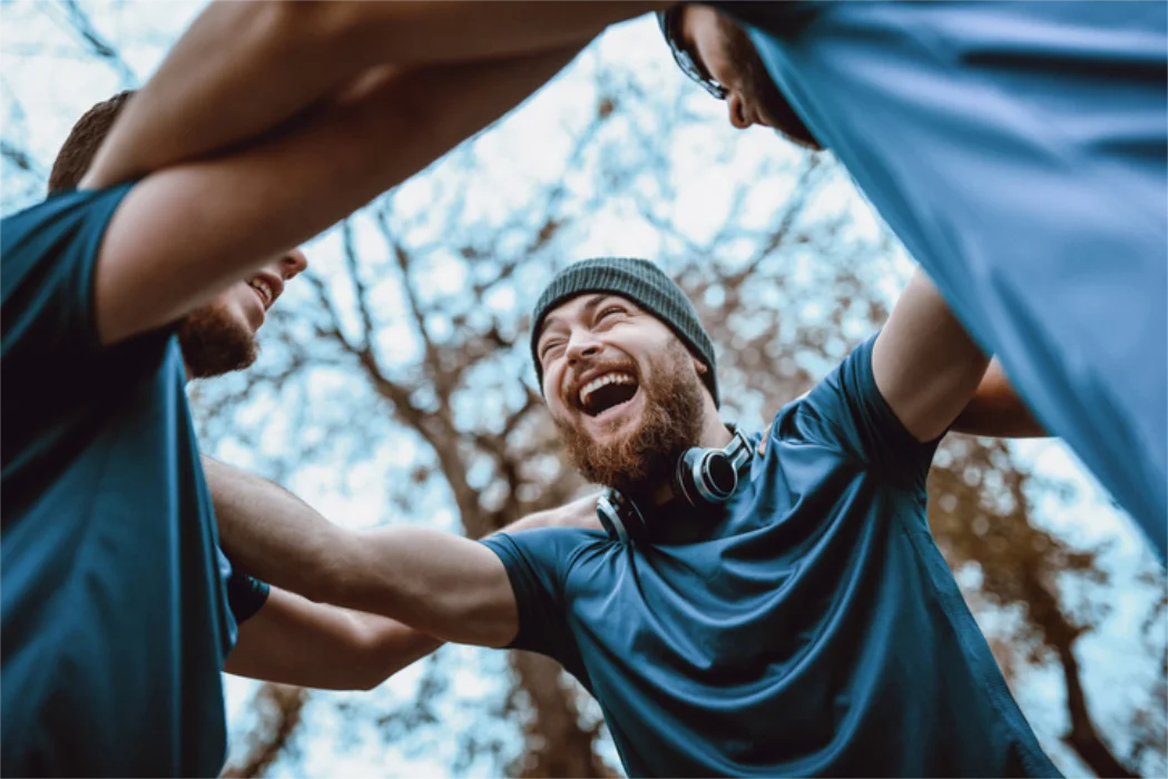 Happy group of men in athletic gear forming a huddle outdoors with trees in the background.