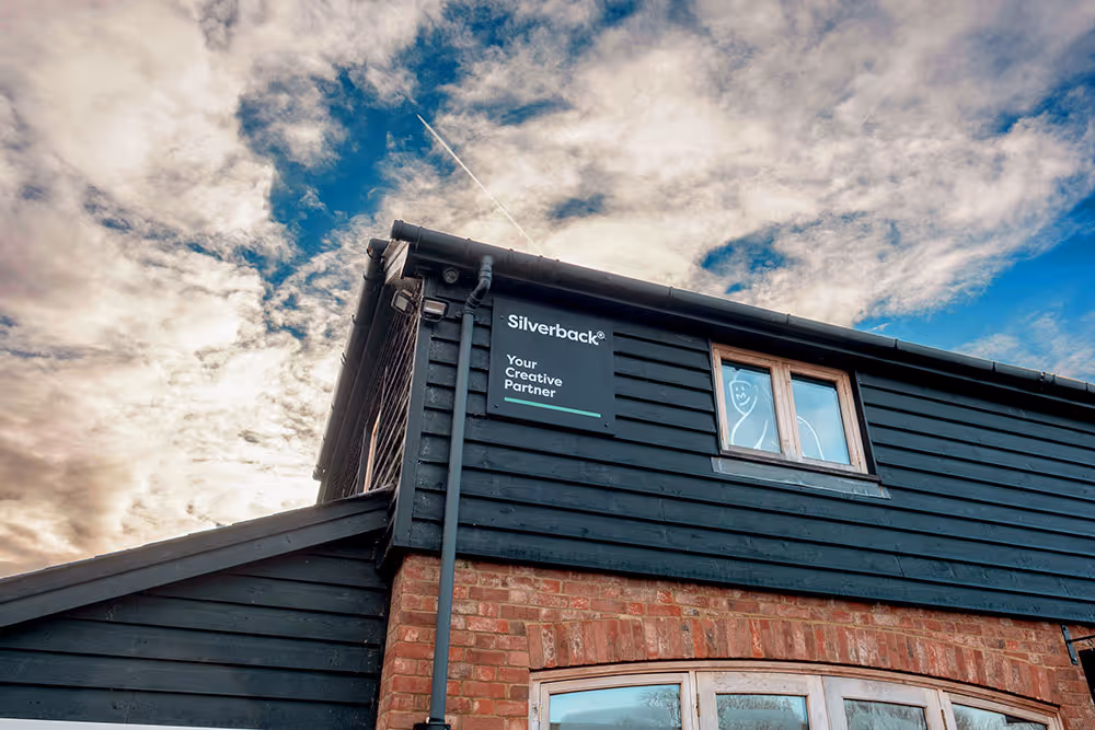 Black wooden building with a Silverback Creative Partner sign and a window featuring a white line drawing of a gorilla face under a cloudy sky.