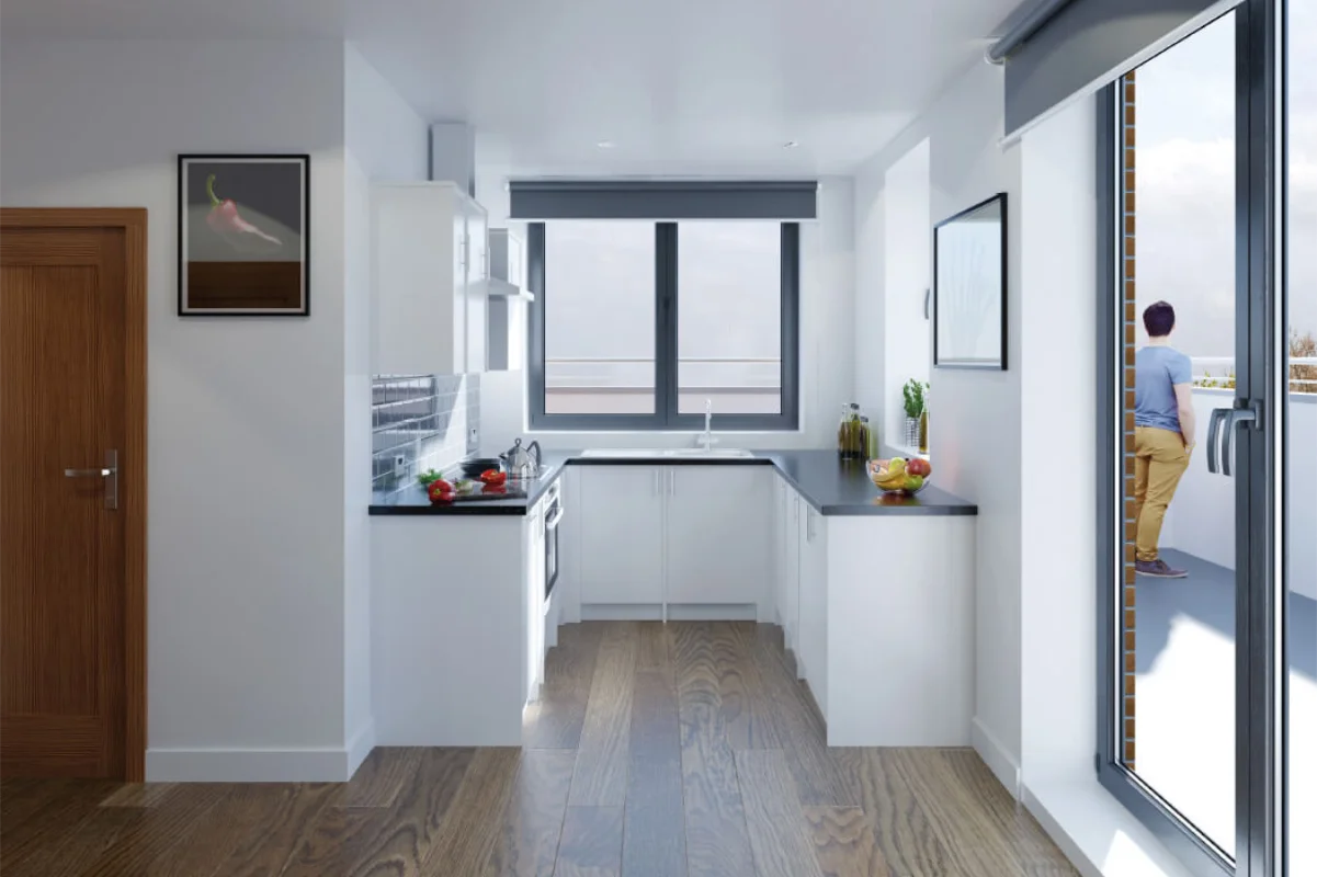 Modern kitchen with white cabinets, black countertops, wooden floor, window above the sink, glass door leading to balcony where a person stands.