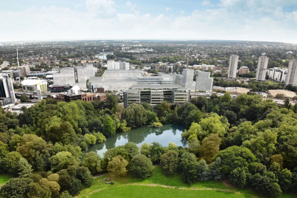 Aerial view of a cityscape with a dense green park and pond in the foreground and urban buildings in the background.