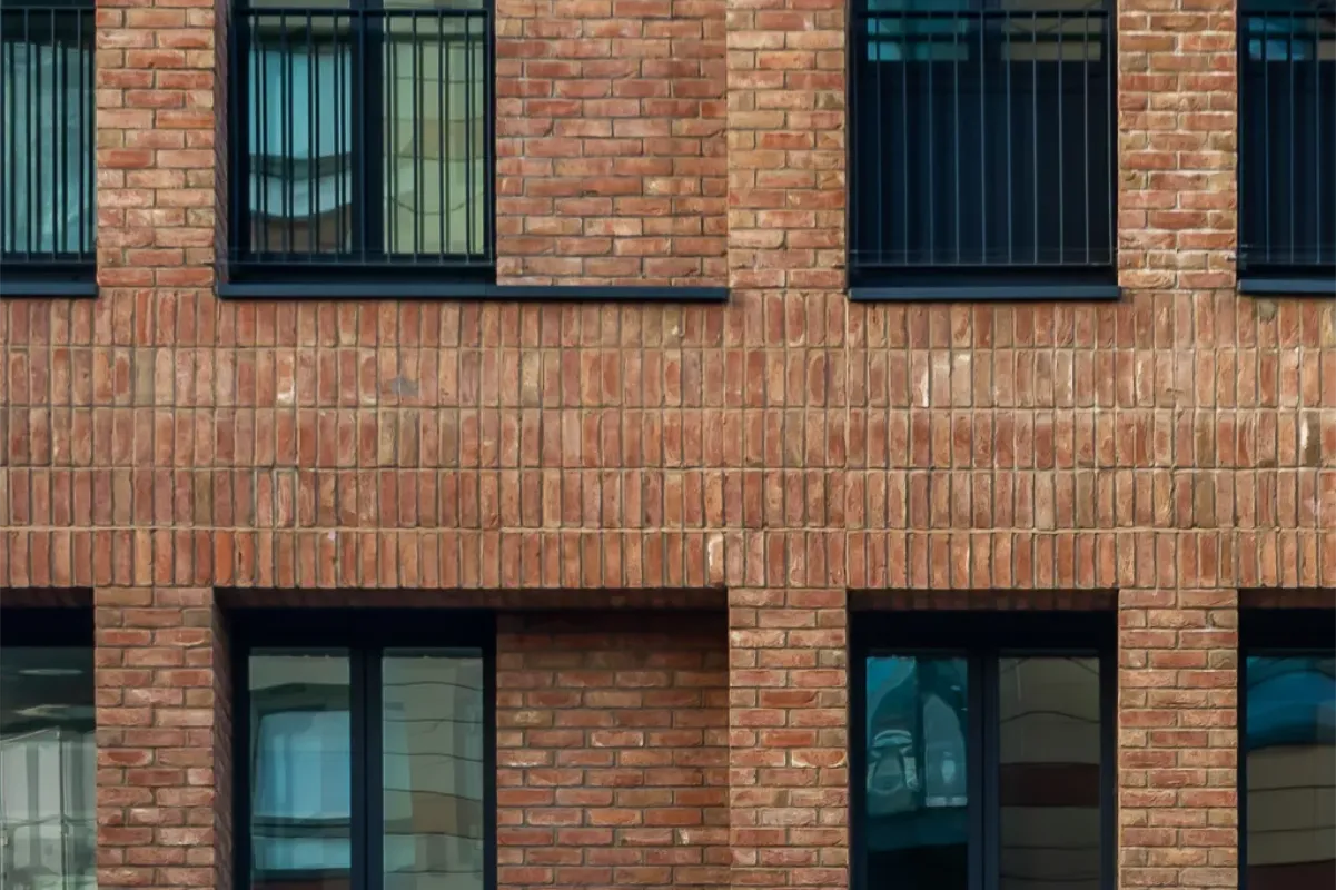 Close-up of a brick building facade with four windows, two on the upper level with black bars and two on the lower level without bars.
