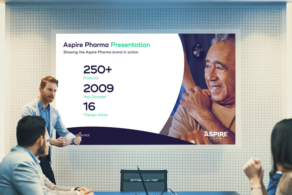 Man in a conference room showing an Aspire Pharma presentation that shows an image of a person next to some statistics.