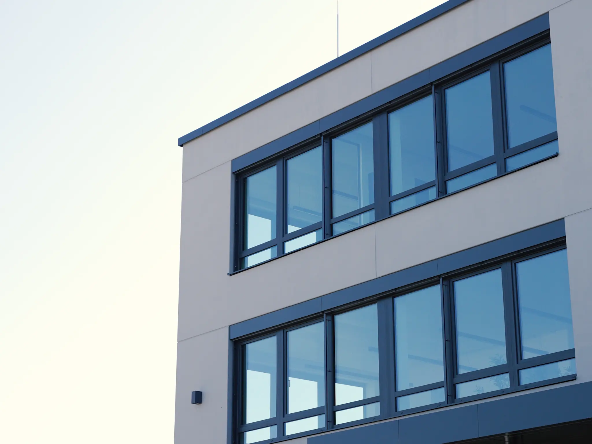 Moderne Gebäudefassade mit großen, rechteckigen Fenstern an einem hellen Bürohaus