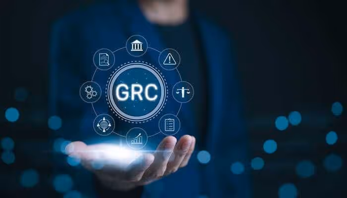 Hand holding a glowing circle with 'GRC' surrounded by governance, risk, and compliance icons on a dark blue background.