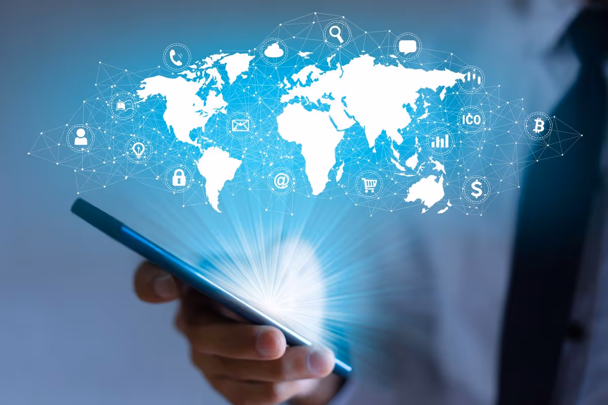 Hand holding a smartphone emitting a glowing world map with interconnected digital icons representing global communication and technology.