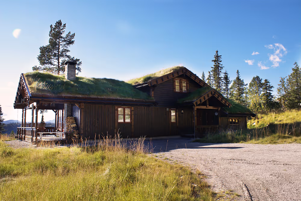 Ein traditionelles Holzhaus mit begrüntem Dach in einer ländlichen Landschaft unter blauem Himmel.