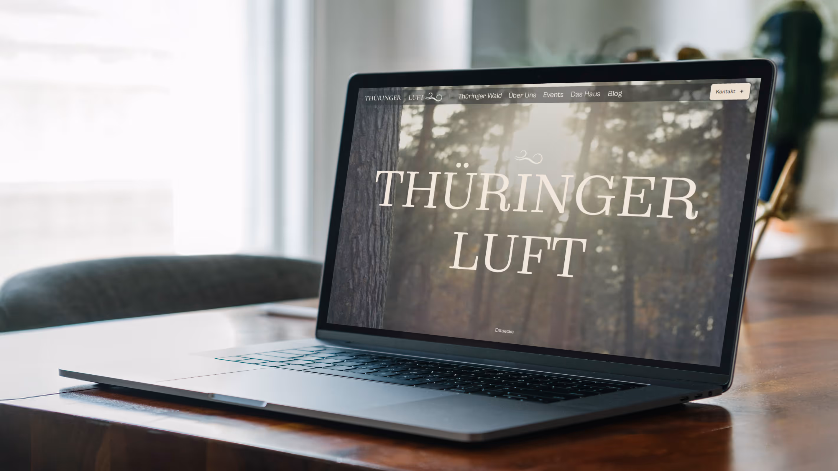 Ein aufgeklappter Laptop auf einem Holztisch zeigt eine Webseite mit der Überschrift 'THÜRINGER LUFT' vor einem Hintergrund mit Bäumen.