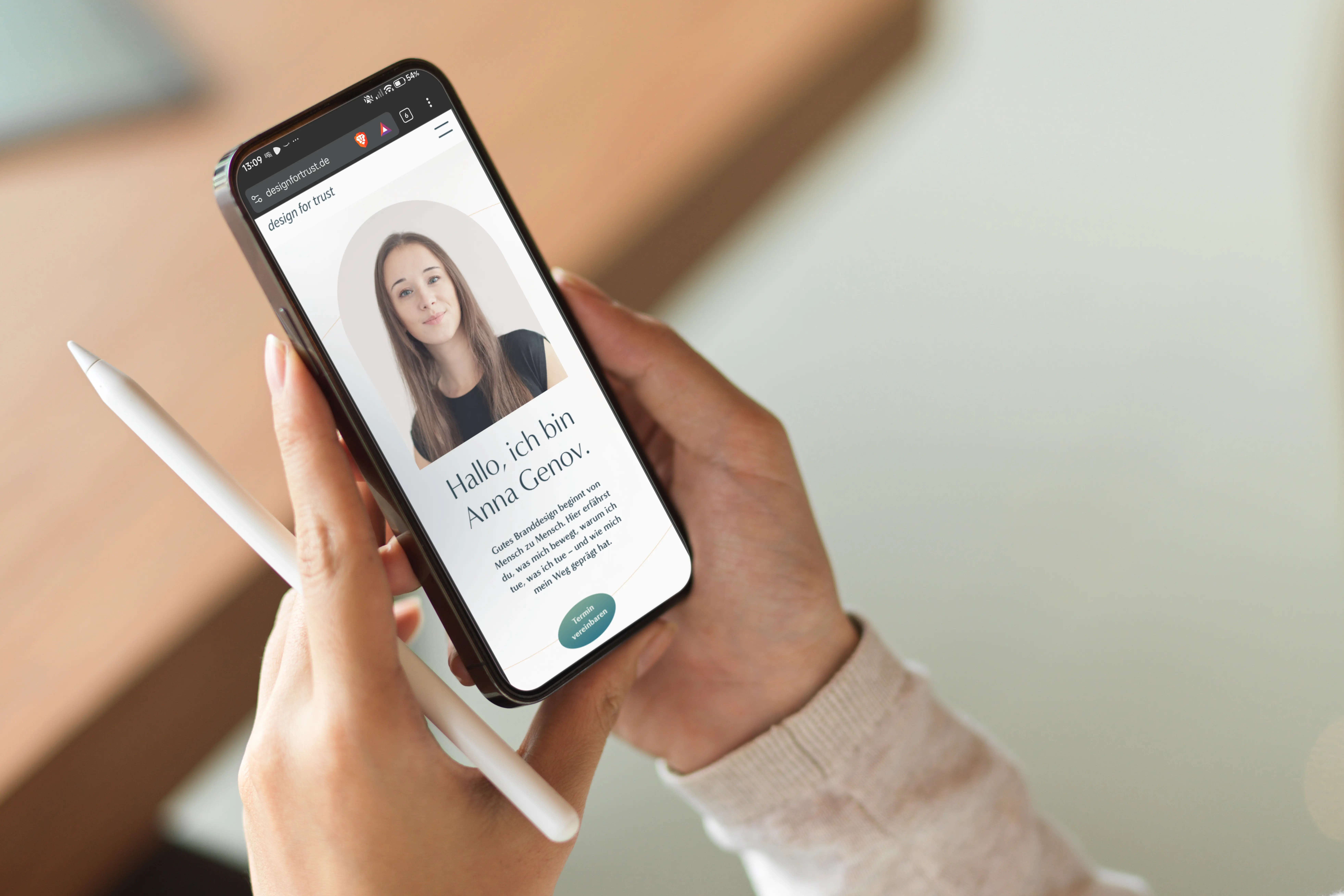 Eine Person hält ein Smartphone und einen weißen Stylus, auf dem Bildschirm ist die Webseite von Anna Genov mit ihrem Porträt und Willkommensnachricht zu sehen.