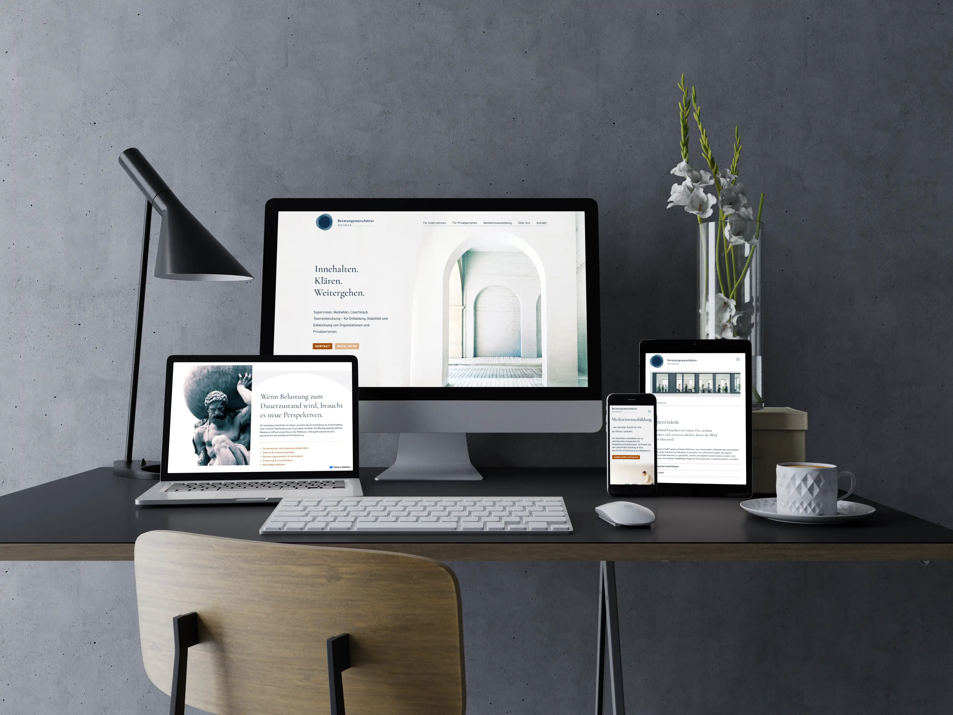 Moderner Schreibtisch mit Computer, Laptop, Tablet und Smartphone, die alle eine Beratungswebsite anzeigen, neben einer weißen Kaffeetasse und einer Vase mit weißen Blumen.