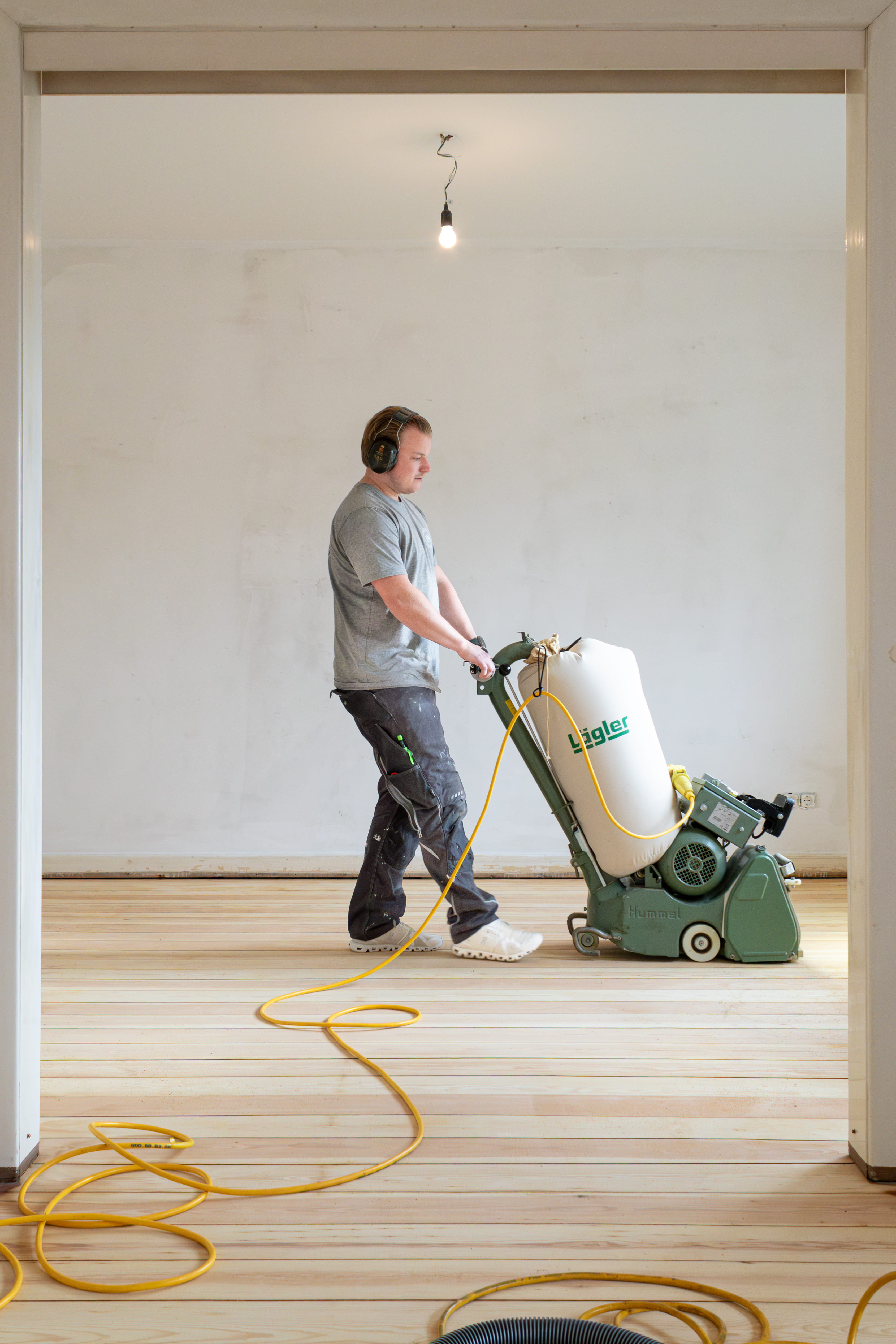 Handwerker schleift Dielen mit Bodenschleifmaschine | Professionelle Bodenverlegung in Hamburg