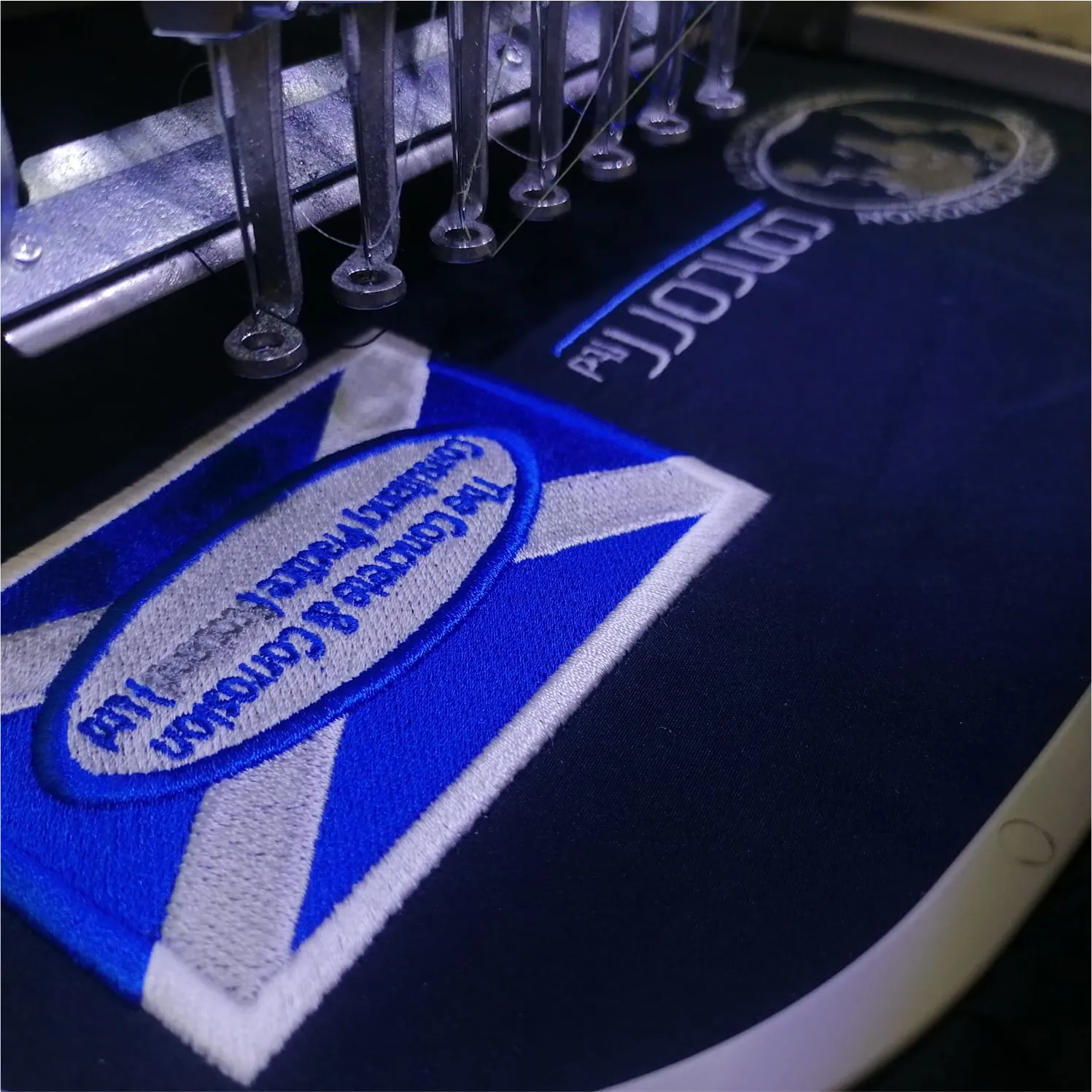 Embroidery machine creating blue and white logo on dark fabric