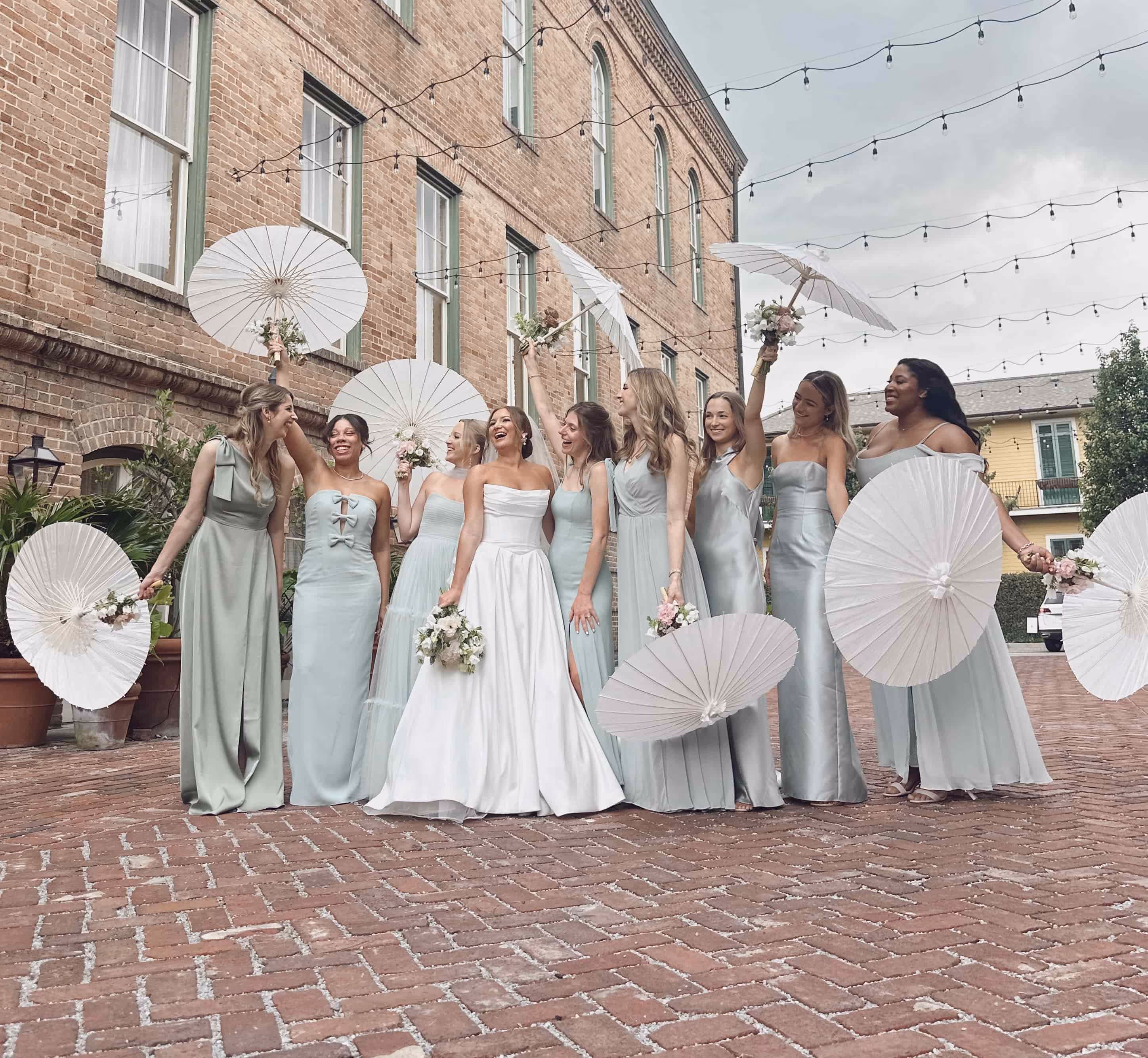 A smiling wedding party in beautiful, green gowns and second-line umbrellas surrounds the bride all dressed in white.