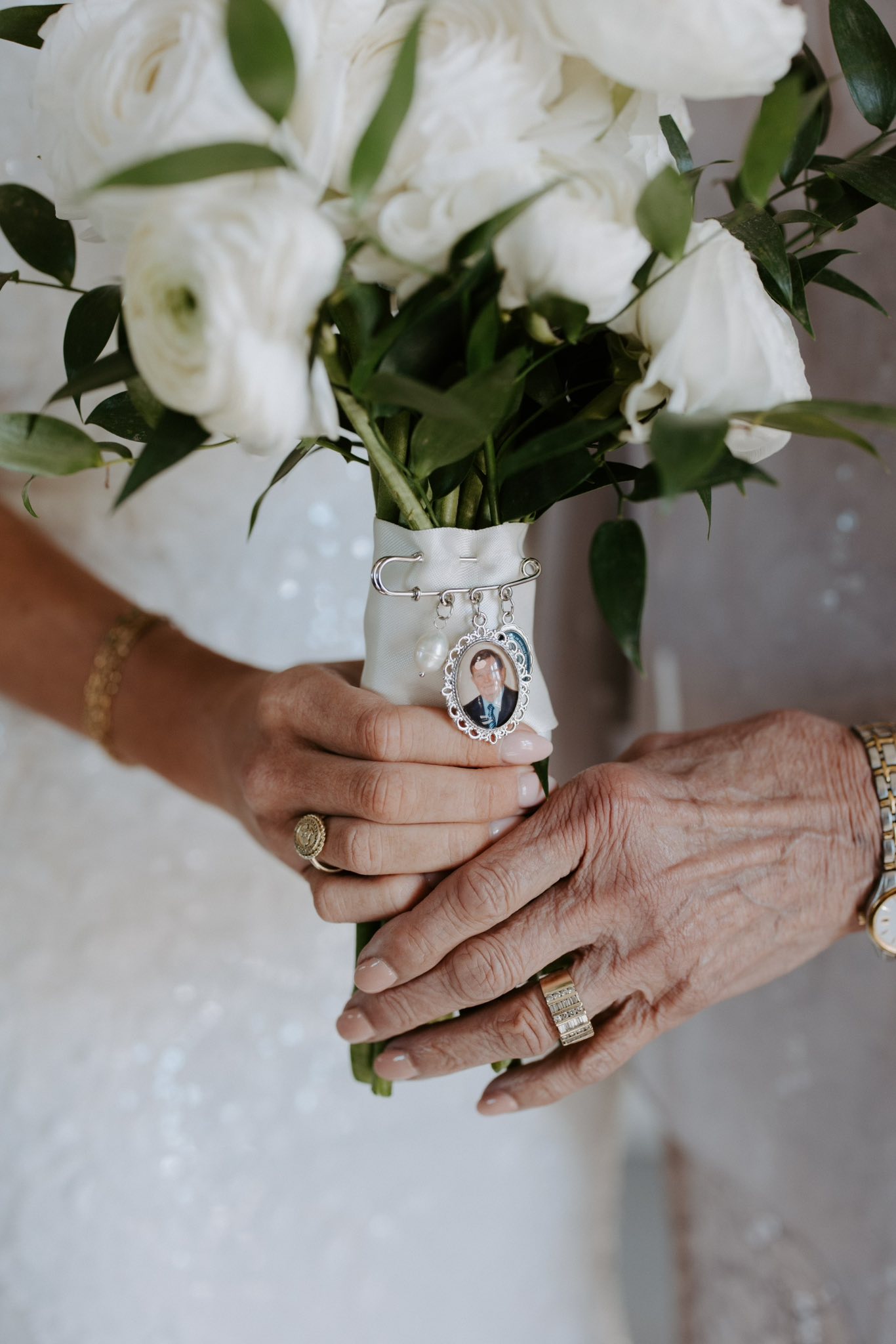 A bride and her mother holding a vase of flowers together, hand in hand.