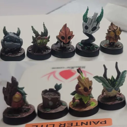 Ten small detailed fantasy miniatures arranged in two rows on a white surface, each resembling different animated characters with features like horns, leaves, and wooden textures.