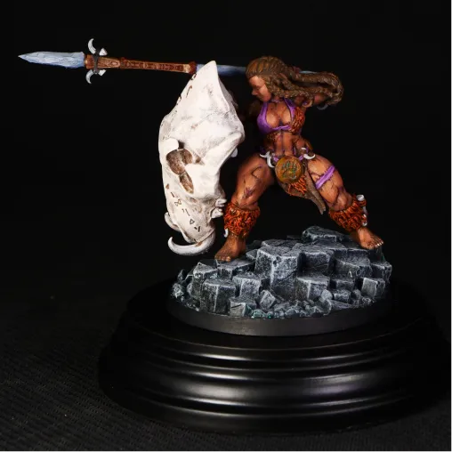 Painted miniature figure resembling a dark, twisted tree-like creature with orange glowing bulbous growths and sharp wooden branches as limbs, standing on a rocky base decorated with small skulls, placed on a colorful gaming mat with a computer keyboard, monitor, and speaker in the background.