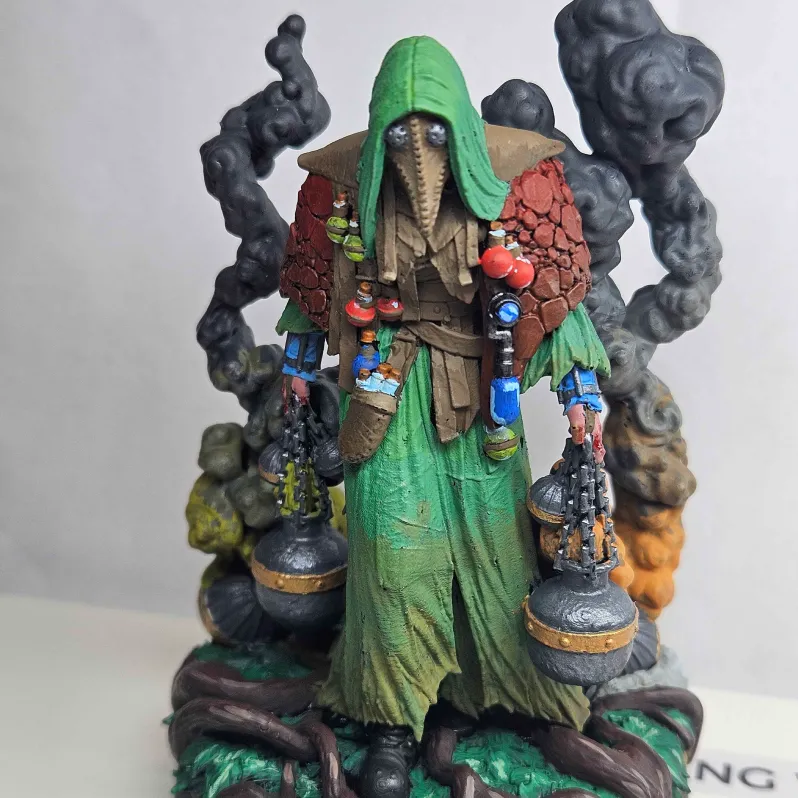 Painted figurine of a hooded character wearing a green robe and a brown, textured cloak with a plague doctor style mask, holding two spherical containers emitting smoke.