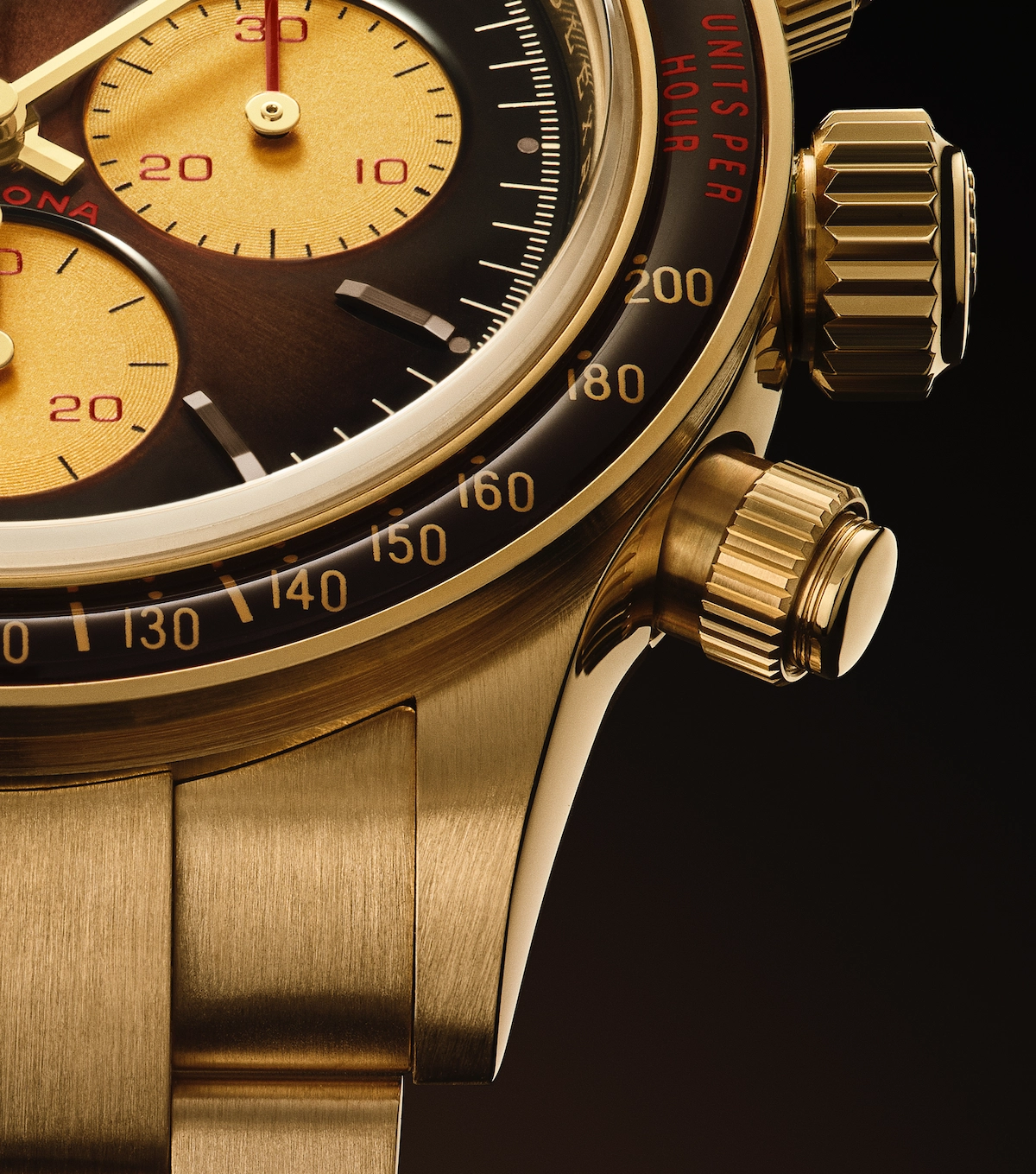 Close-up of a gold chronograph wristwatch with detailed tachymeter bezel and two pushers on the side.
