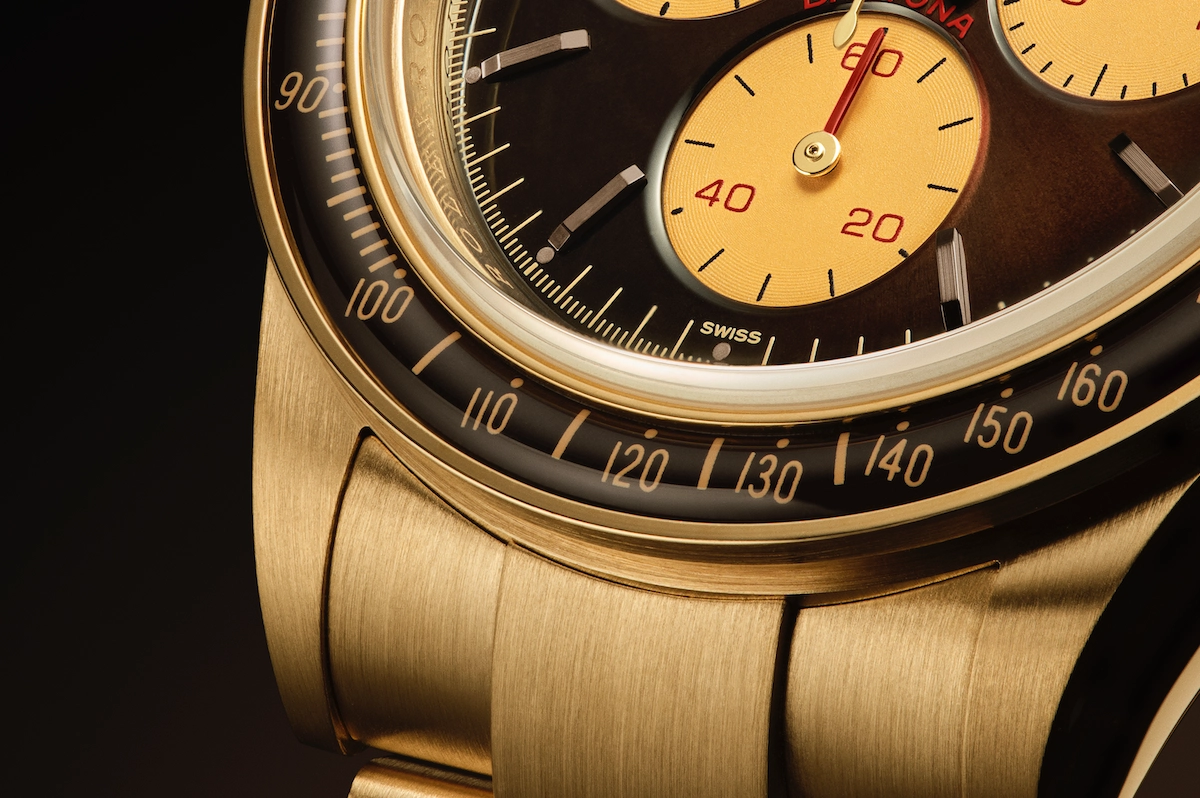 Close-up of a luxury gold watch with a black bezel marked with numbers and a dial featuring yellow subdials and red accents.