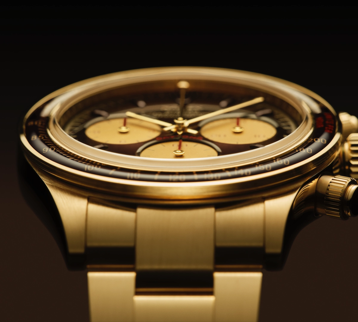 Close-up of a gold wristwatch with three subdials and a black tachymeter bezel on a gold bracelet.