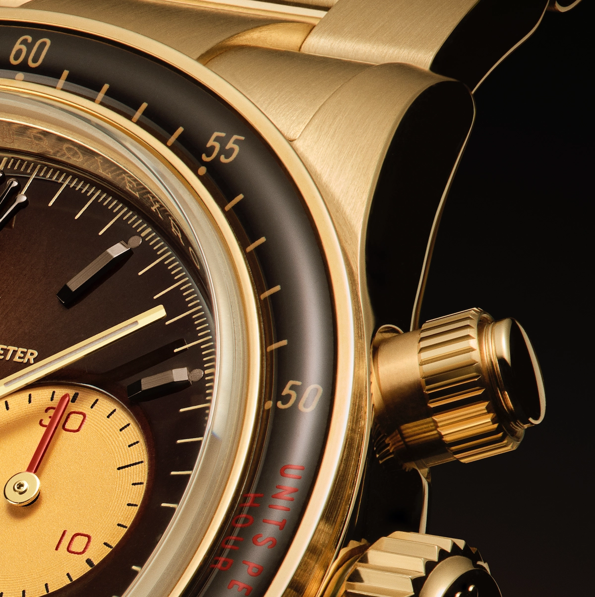 Close-up of a gold wristwatch showing the tachymeter scale, chronograph dials, and textured pushers.
