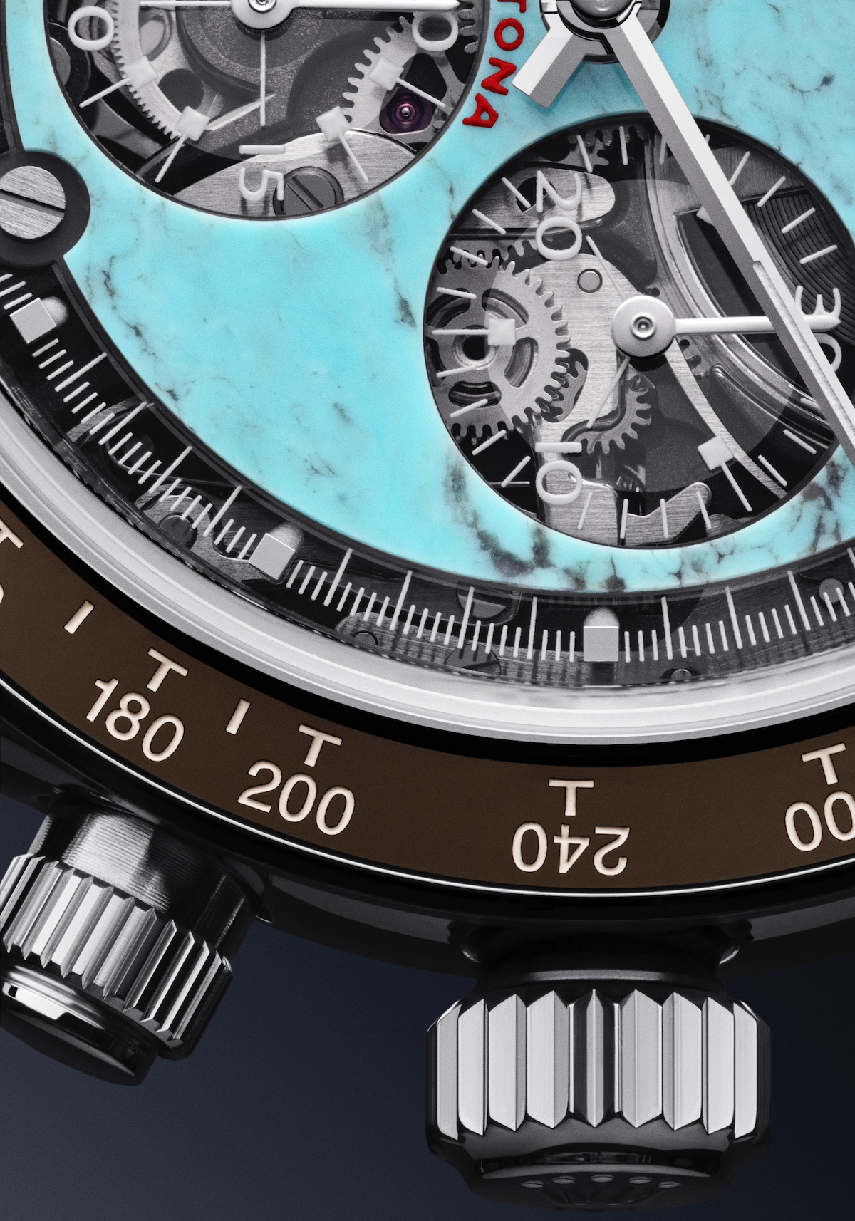 Close-up of a luxury watch face with visible gears, turquoise dial, two silver pushers, and a tachymeter scale on the bezel.