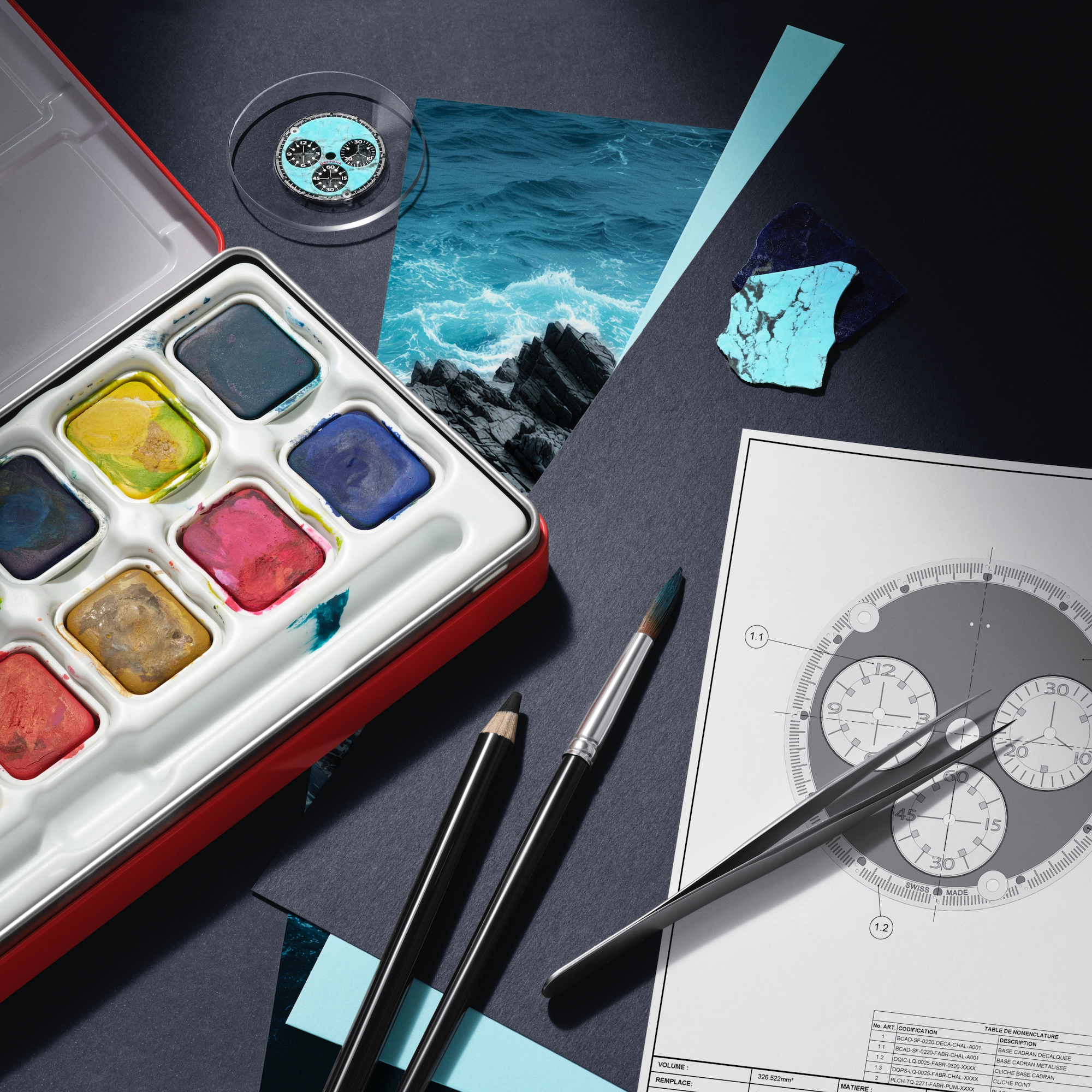 Art supplies including a watercolor palette, paintbrush, pencil, tweezers, watch face blueprint, and fragments of blue stone on a dark surface.