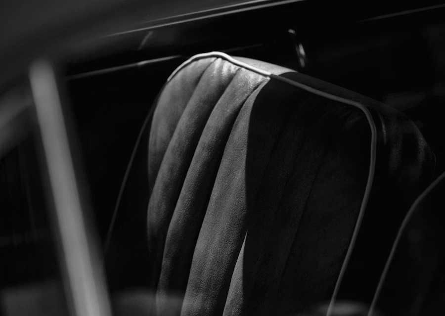 Close-up of a vintage car's leather seat with vertical stitching and piping detail in black and white.