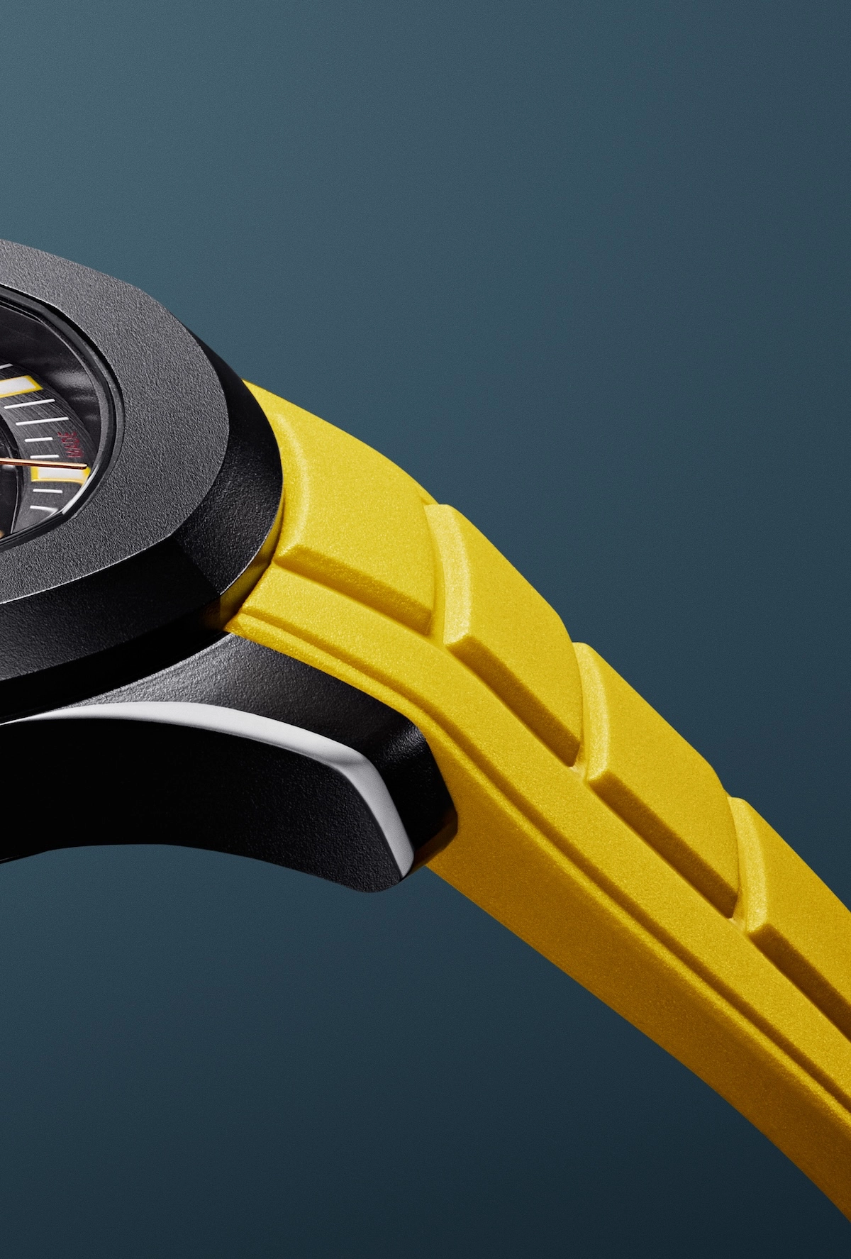 Close-up of a yellow rubber watch strap attached to a black watch case against a blue background.