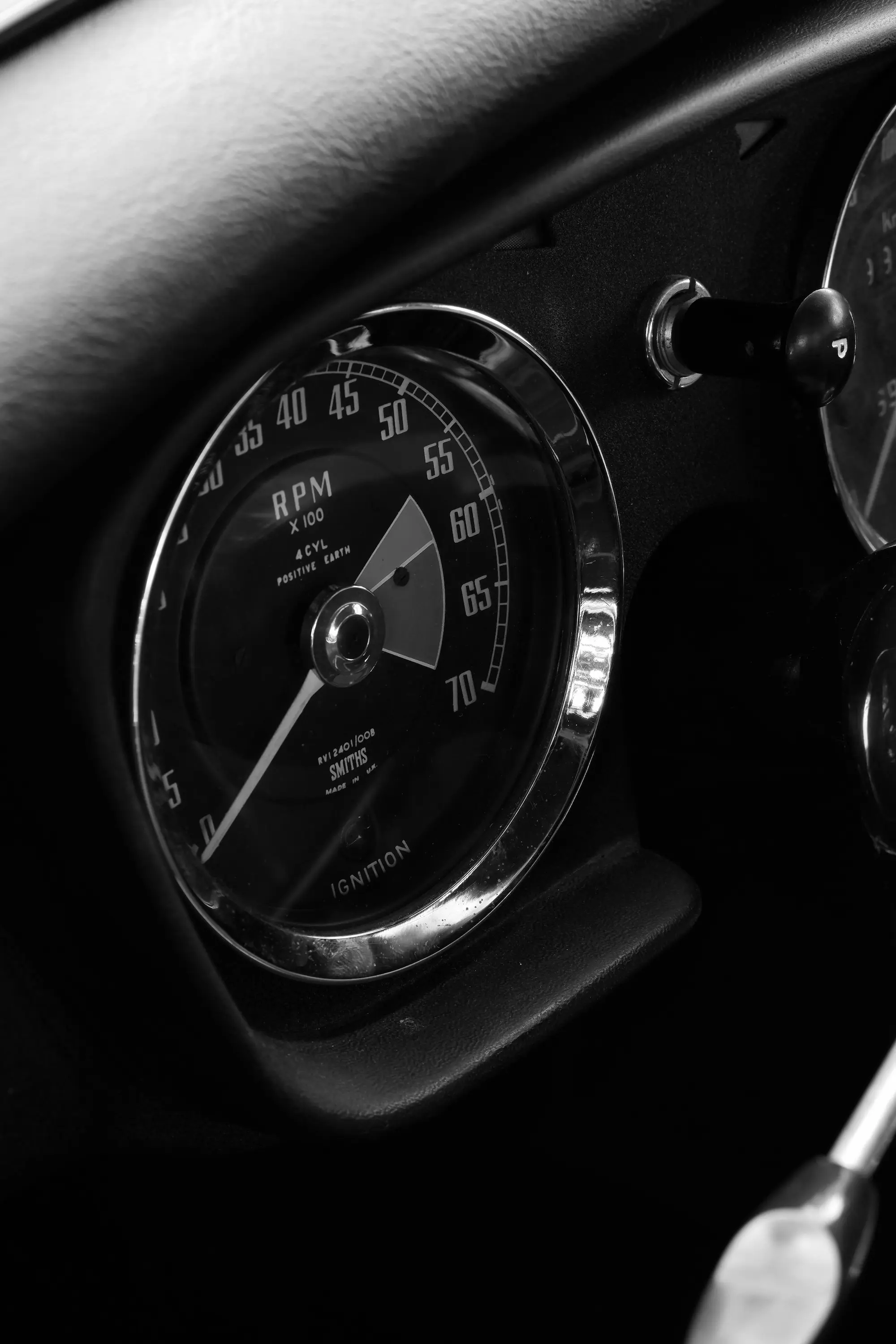Close-up of a vintage car tachometer showing RPM with chrome bezel in black and white.