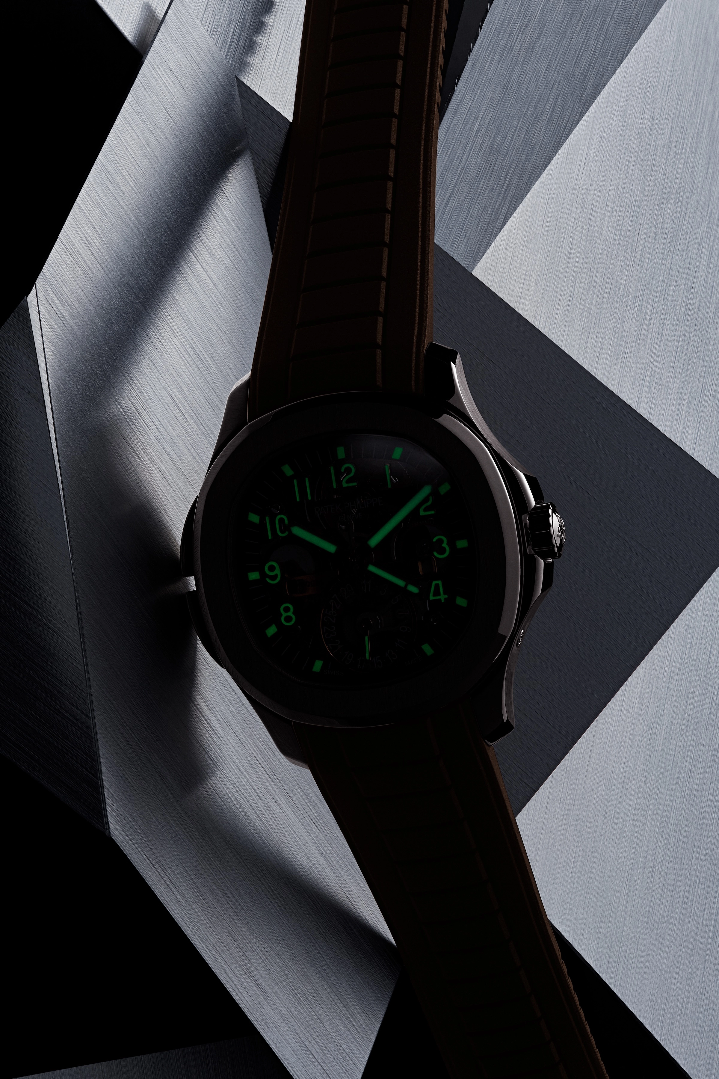 Dark watch with glowing green numbers and hands on a silver geometric background.
