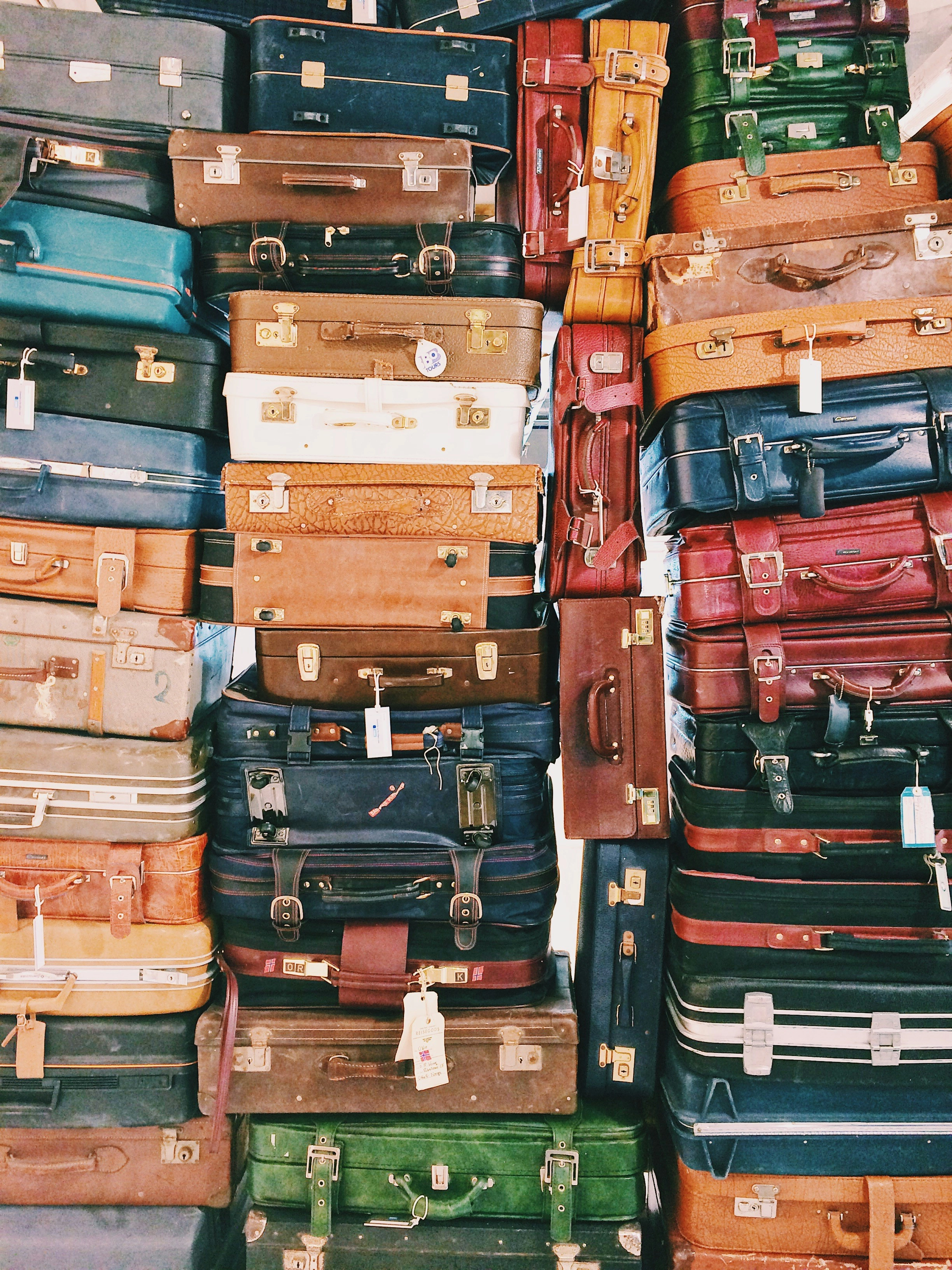 Stack of various vintage suitcases in assorted colors and styles piled up closely together.