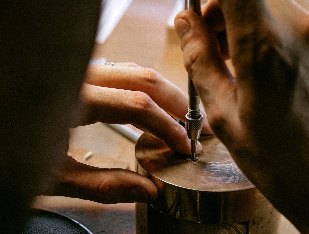 Craftsman using a tool to engrave or work on a small metal watch component.