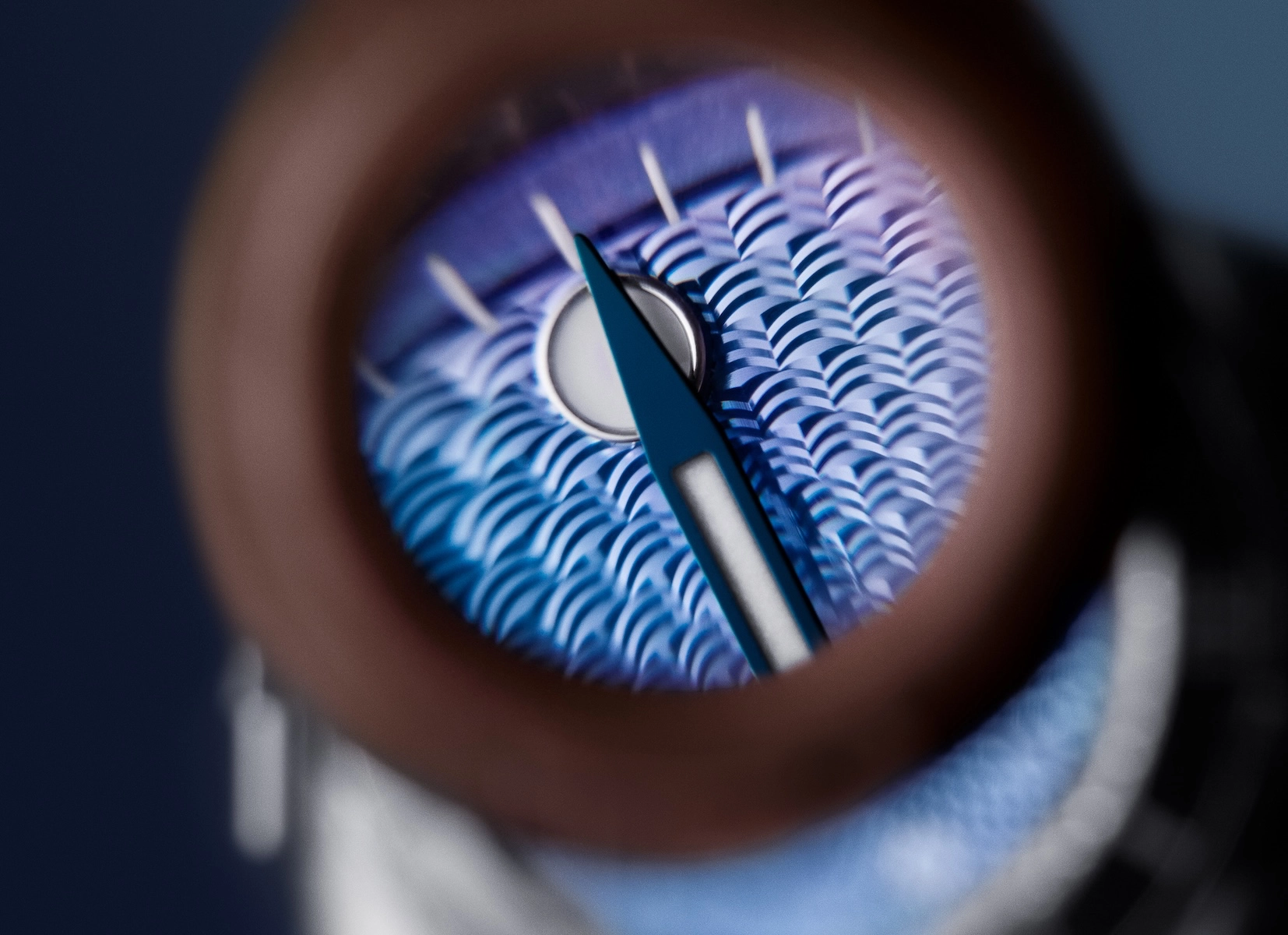 Close-up of blue watch hands over a detailed guilloché patterned dial under magnification.