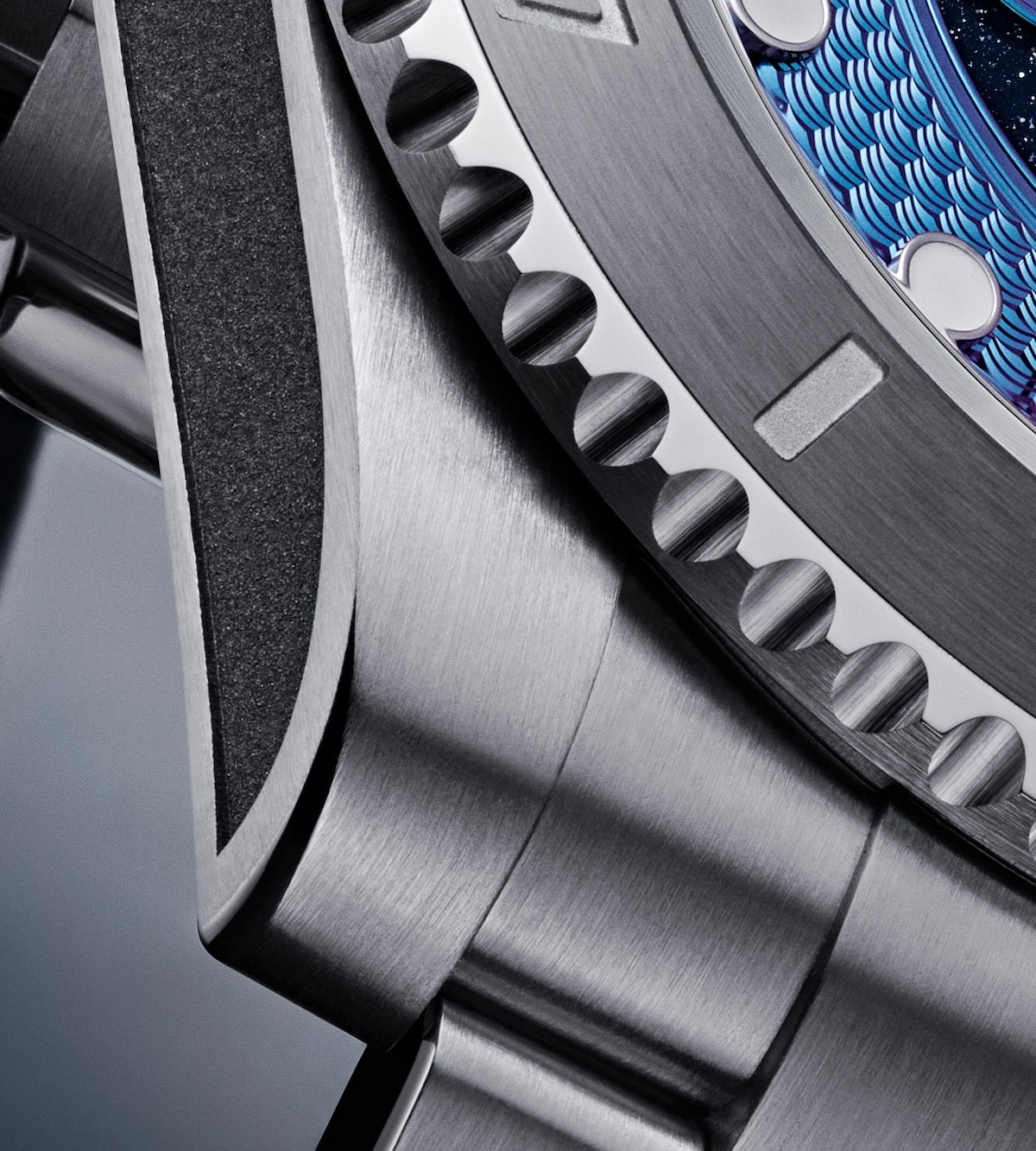 Close-up of a stainless steel watch bezel and strap with blue textured watch face edge.