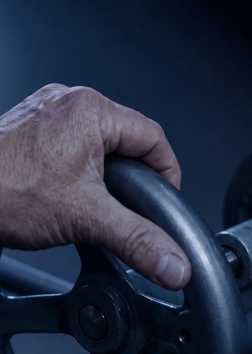 Close-up of a hand gripping a black industrial valve wheel against a dark background.