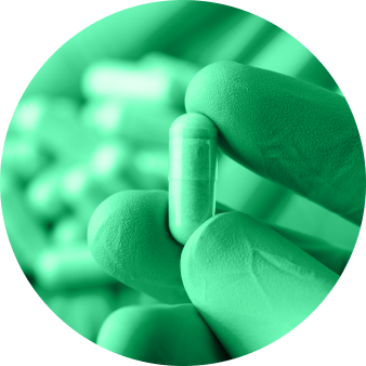 Gloved hand holding a single capsule pill with more capsules blurred in the background.