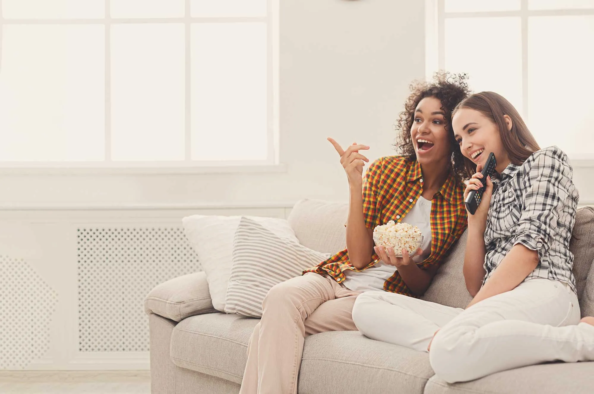 Two women sitting on a couch and pointing at something.