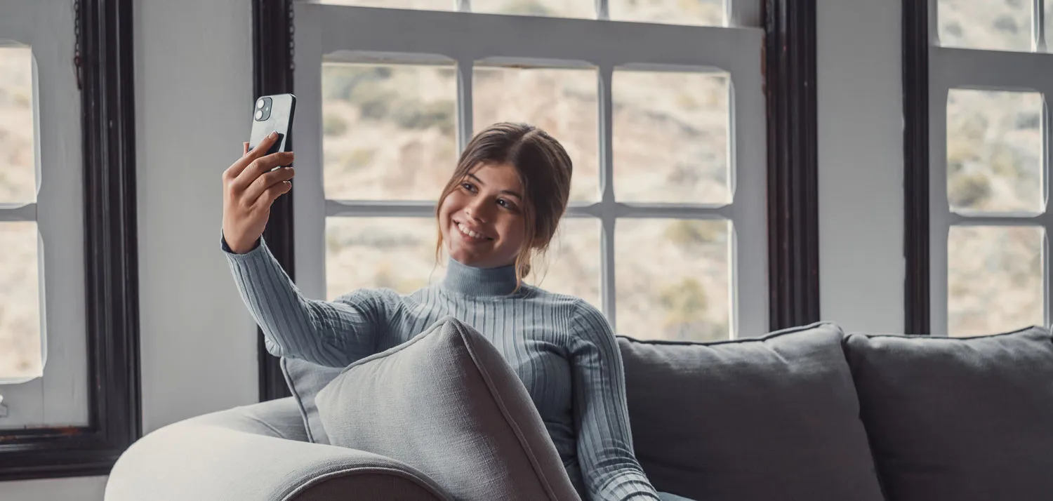 A woman sitting on a couch taking a selfie with her phone.