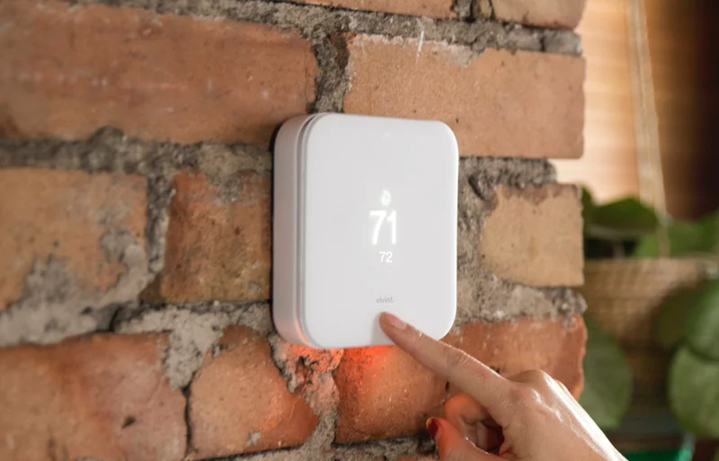 A person pointing at a thermostaer on a brick wall.