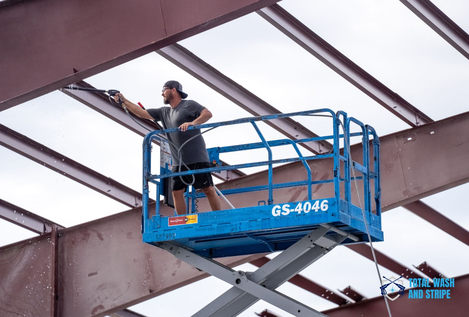 Commercial pressure washing technician cleaning steel beams from a scissor lift