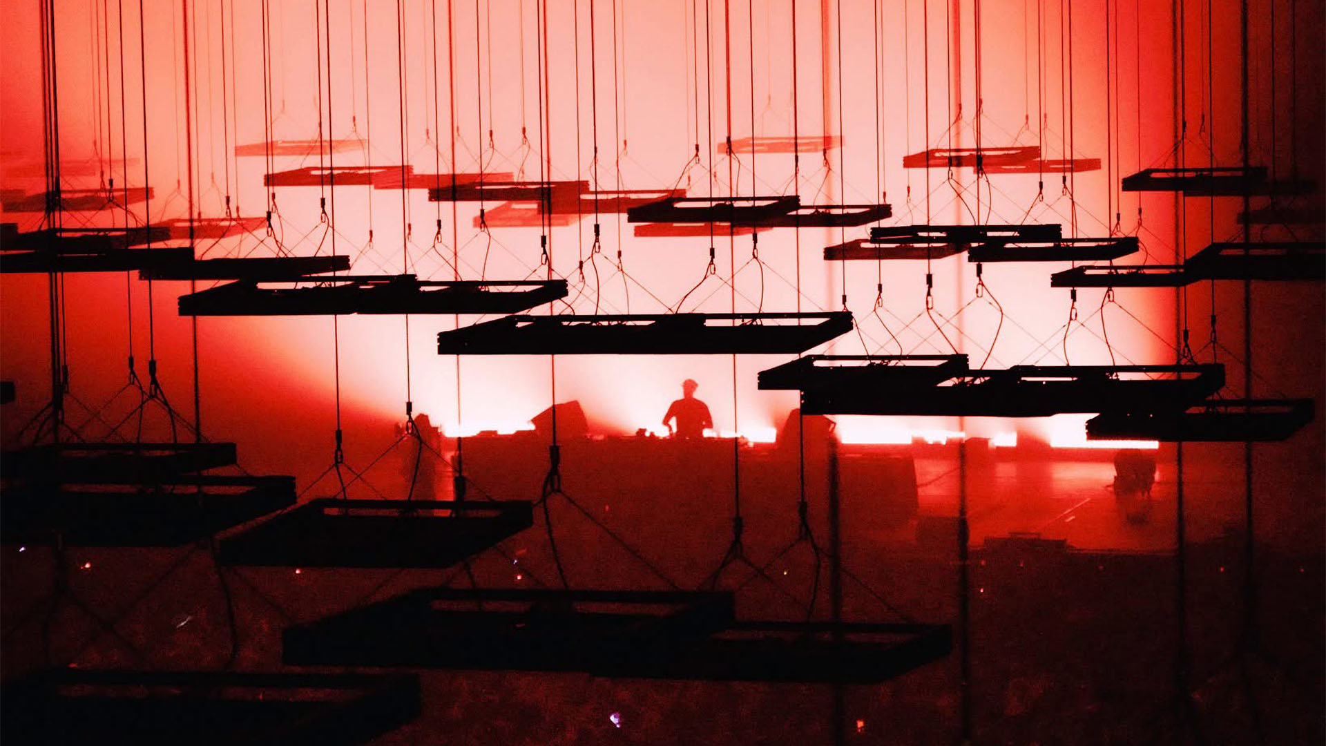 Suspended rectangular panels arranged at different heights in a red-lit stage installation