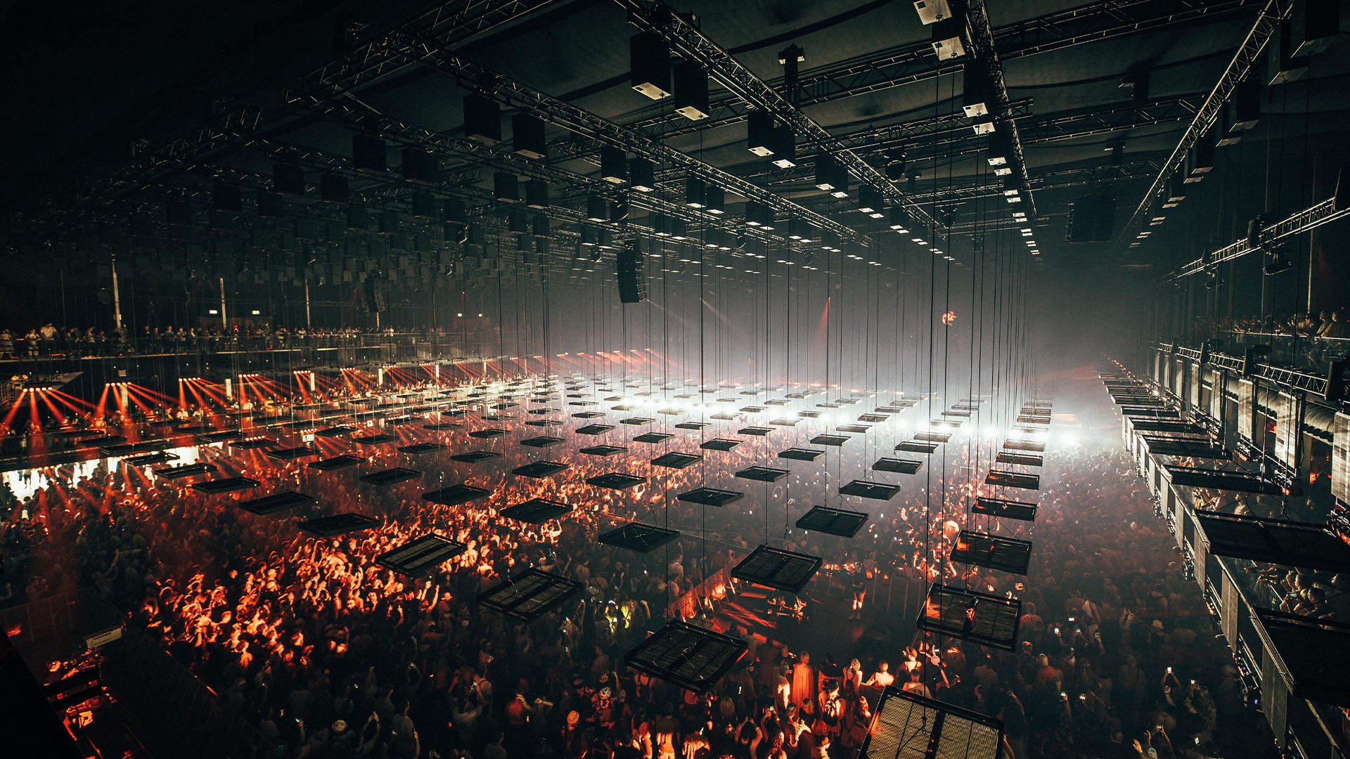 Overhead view of suspended rectangular panels and rigging above a concert audience