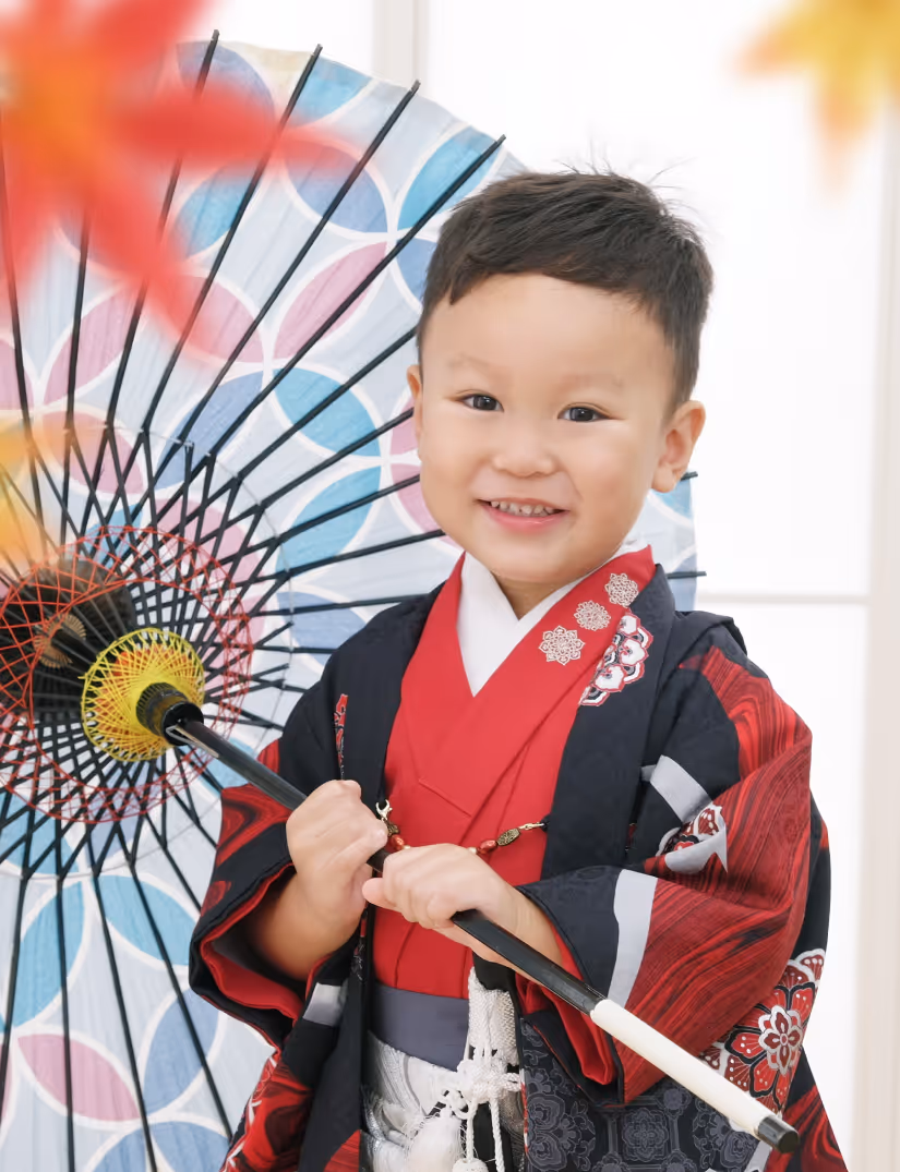 Smiling young boy wearing traditional Japanese kimono holding a colorful parasol.