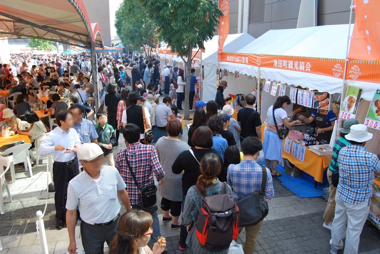 Crowd of people lining up and sitting under tents at an outdoor market with food stalls.