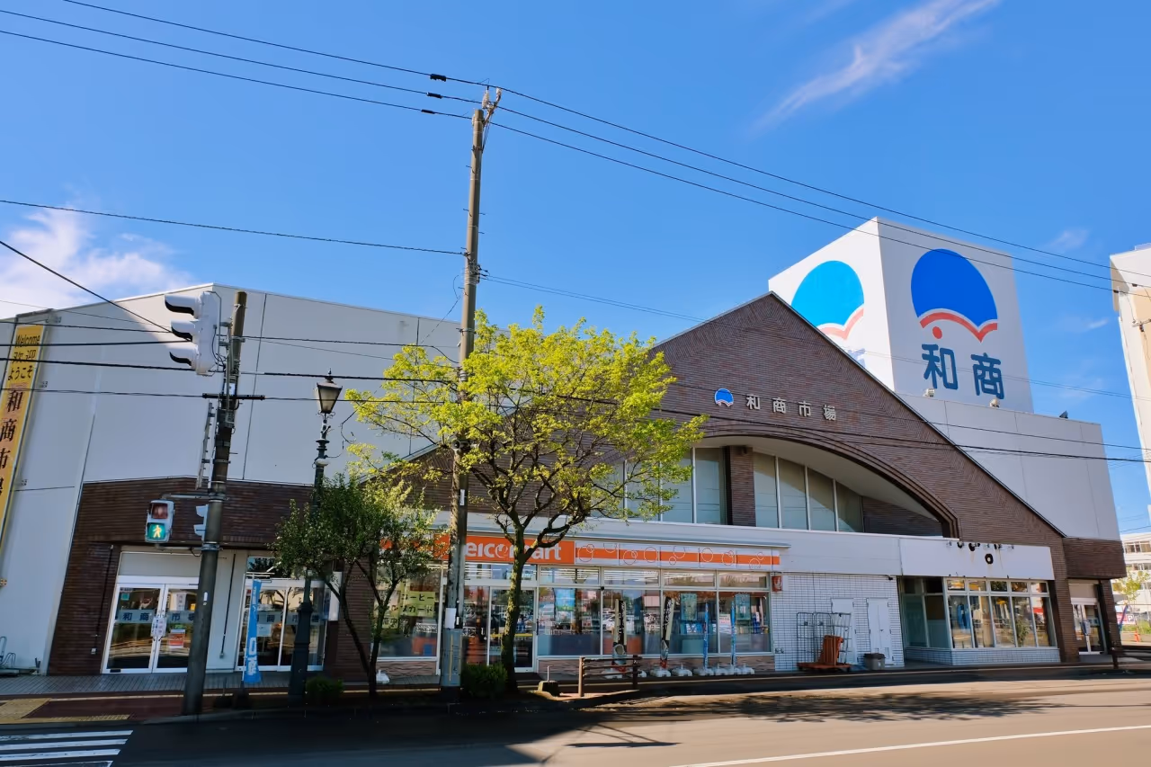 Exterior of a brick and white building with Japanese signage and a convenience store under a clear blue sky.