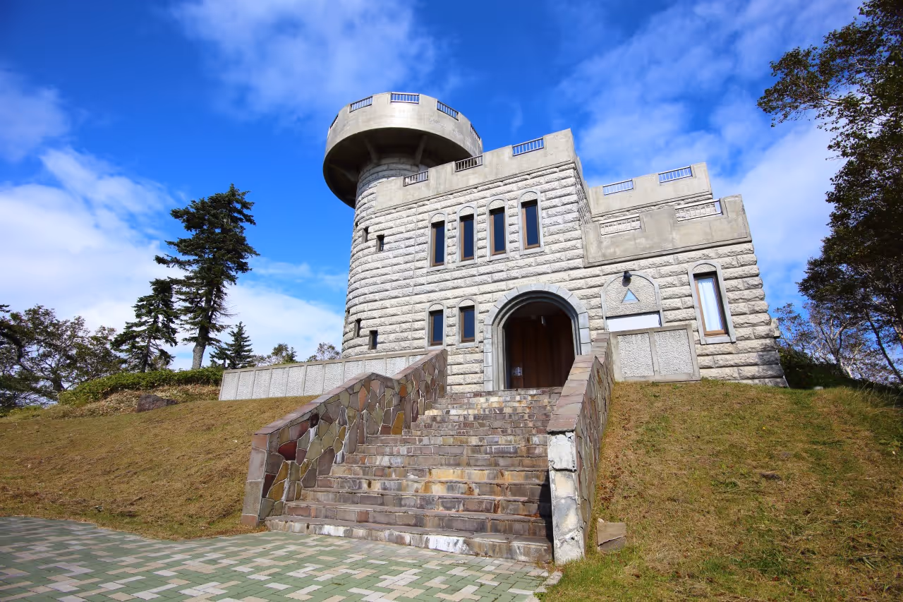 Stone observation facility with a cylindrical tower and arched entrance, set on a grassy hill under a blue sky.