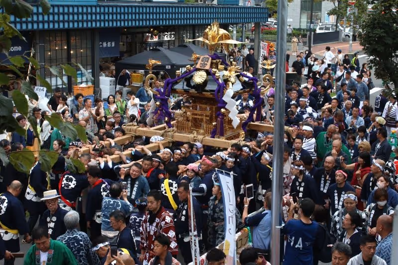 Crowd of people participating in a traditional Japanese festival carrying a decorated mikoshi shrine through a city street.