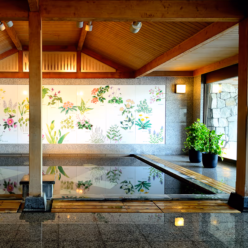 Indoor Japanese onsen bath with wooden beams, botanical illustrations on wall, and potted plants by a large window.