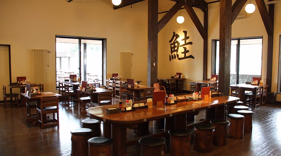 Interior of a Japanese-style restaurant with wooden tables and stools, soft lighting, and a large kanji character on the wall.